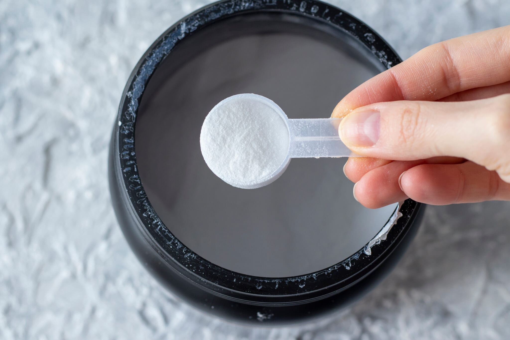 Catalyst-Fitness-Close-up of a woman's hand with a measuring spoon of white BCAA powder. Protein shake for athletes and athletes